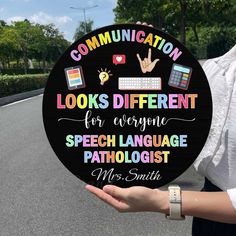 a woman holding up a sign that says communication looks different for everyone speech language pathologist mrs smith