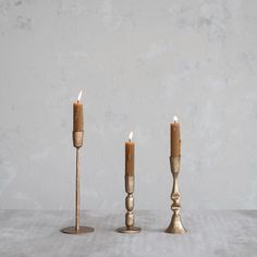 three candles are standing next to each other on a table in front of a concrete wall