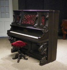 an old piano sitting in the middle of a room with a red chair next to it