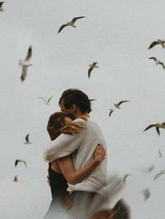 two people embracing each other with birds flying in the background