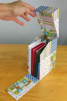 a hand is opening an open book on a wooden table with many different colored papers