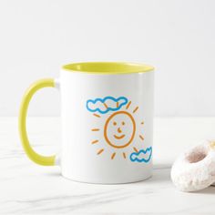 a white and yellow coffee mug sitting next to a donut