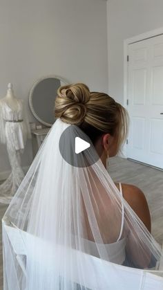 a woman wearing a wedding veil with her hair in a bun and looking into the mirror