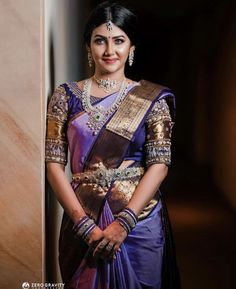 a woman in a purple and gold sari standing next to a wall with her hands on her hips