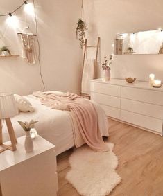 a bedroom with white furniture and lights on the wall, along with a bed covered in a pink blanket