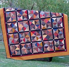 a large quilt is hanging from a tree in the grass, with trees behind it