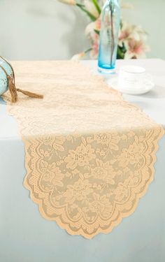 a lace table runner on top of a table next to a blue vase with flowers