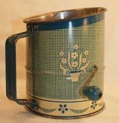 an old blue and white coffee mug with a green handle on the side, next to a metal ball