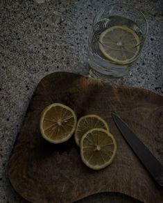 sliced lemons sit on a cutting board next to a knife and glass of water