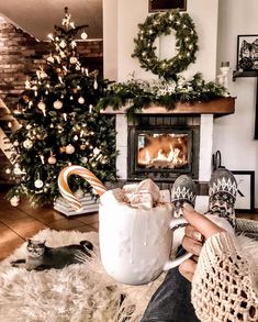 a person holding a mug in front of a fireplace with christmas decorations on the mantle