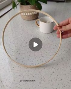 someone is holding a cup in front of a circular object on a table with a plant behind it