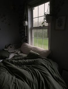 an unmade bed sitting next to a window in a room with dark walls and green sheets