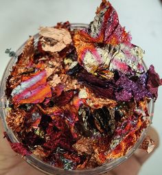 a hand holding a bowl filled with different types of dried flowers in it's palm