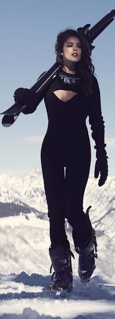 a woman with skis on her back walking in the snow holding two ski poles