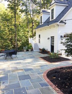 an outdoor patio with flagstone pavers and brick edging in front of a white house