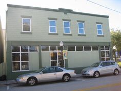 two cars parked in front of a green building with three windows on the second floor