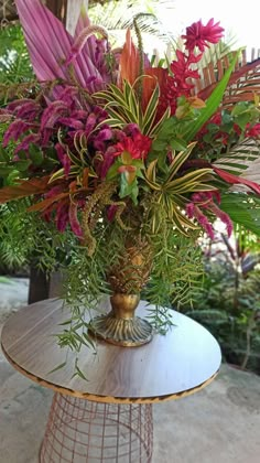 a vase filled with lots of colorful flowers on top of a wooden table covered in greenery