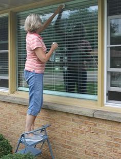 an older woman is painting the window outside