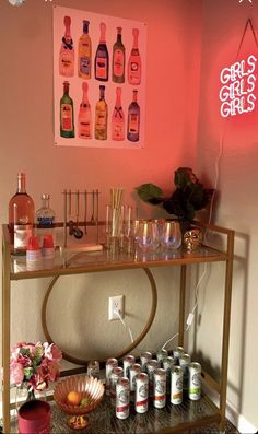 a bar cart with liquor bottles and glasses on it in front of a pink wall