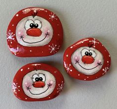 three red and white painted rocks with snowflakes on them, each depicting a smiling clown