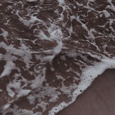 an ocean wave rolls in on the sand at the edge of the beach with white foam