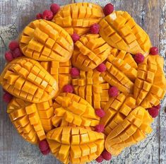 sliced mangos and raspberries arranged in a circle on top of a wooden table