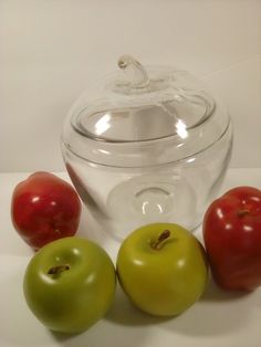 three apples and two tomatoes sitting next to a glass container