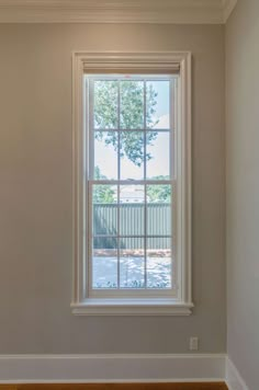 an empty room with a large window and hard wood flooring on the side wall