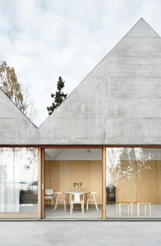 an outdoor dining area with tables and chairs in front of a concrete building that has triangular windows