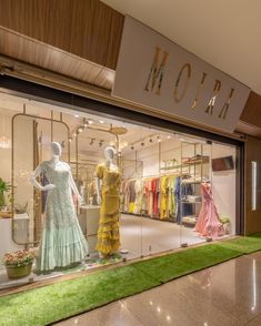 a store front window with mannequins dressed in yellow and green dresses on display