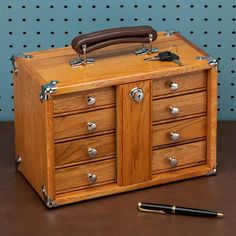 an old fashioned wooden box with drawers and a pen on the table next to it