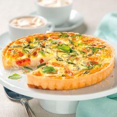 a small quiche on a plate with a fork and cup of coffee in the background