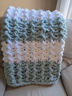 a blue and white crocheted blanket sitting on top of a couch next to a window