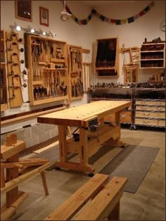 a workbench with lots of tools hanging on the wall and wooden benches in front of it