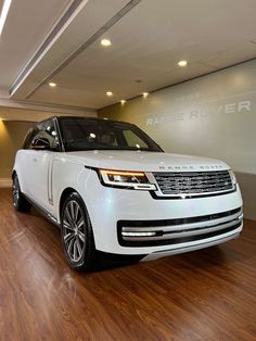 a white range rover parked in a showroom with hard wood flooring and lighting