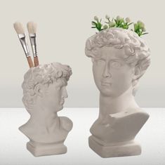 two statues with brushes in their heads and one has flowers on it's head