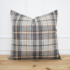 a plaid pillow sitting on top of a wooden floor next to a white and brown wall