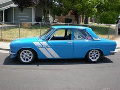 a blue and white car parked on the side of a road next to a fence