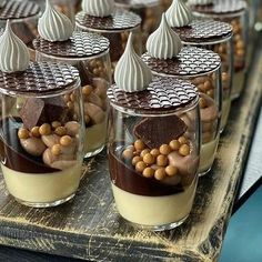 several desserts are arranged in glass cups on a wooden tray with chocolate and nuts