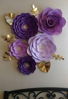 purple paper flowers on a white wall with gold foil leaves in the middle and one large flower surrounded by smaller ones