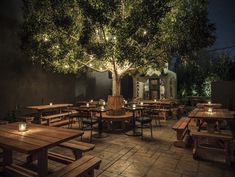 an outdoor dining area with wooden tables and benches lit up by string lights at night