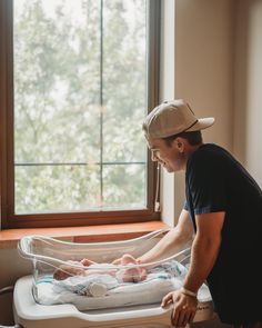 a man standing next to a baby in a crib with a window behind him