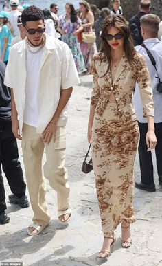 a woman in a dress and sunglasses walking next to a man wearing a white shirt