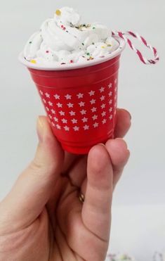 a hand holding a red cup with whipped cream and sprinkles on top