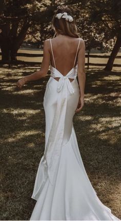 the back of a woman in a white wedding dress standing on grass with trees behind her