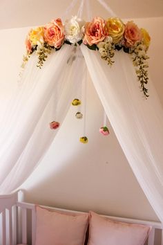 a canopy bed with pink and yellow flowers hanging from it's sides over the headboard