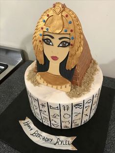 an egyptian themed birthday cake with gold and blue decorations on it's head, sitting on a black countertop