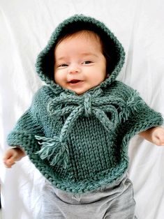 a baby wearing a green knitted sweater and matching pants with a hood on it's head