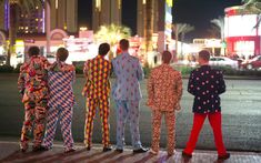 four men in colorful pajamas are standing on the sidewalk and looking at the city lights