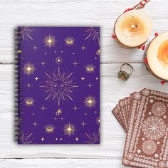 a purple notebook with gold stars on it next to two candles and other items that include cards